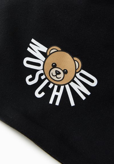 Svart stoff med en stilisert brun bjørn grafikk med et rundet ansikt, ledsaget av teksten "MOSCHINO" i hvite, fete bokstaver.