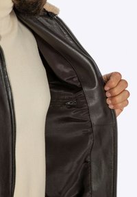 Bruine leren jas met een satijnen binnenkant; voorzien van een zak met rits en een zachte kraag. Binnenvoering in een lichte kleur.