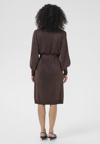 Robe en maille métallique marron avec manches longues, taille cintrée et ourlet au niveau des genoux. Le tissu a un léger éclat et une texture lisse.