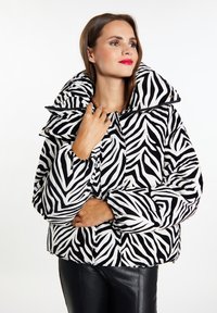 Veste matelassée à imprimé zèbre en noir et blanc, avec un col montant, des détails de boutons et des poignets élastiques ; fabriquée en tissu matelassé.