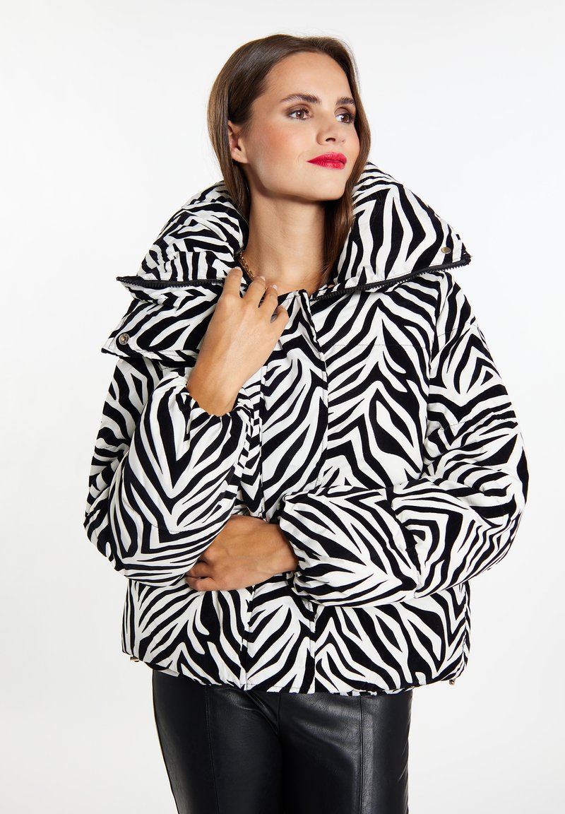 Veste matelassée à imprimé zèbre en noir et blanc, avec un col montant, des détails de boutons et des poignets élastiques ; fabriquée en tissu matelassé.