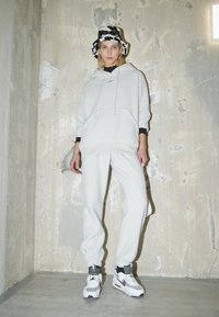 Ljusgrå huvtröja med framficka, matchande med svettbyxor. Svarta detaljer vid ärmsluten. Vita och gråa träningsskor.