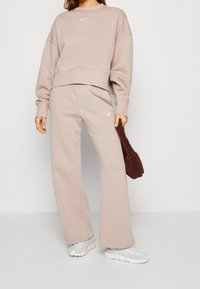 Ljusrosa Nike sweatshirt med croppad design, avslappnad passform och vit logga. Matchande vida sweatpants i samma färg. Mjuk textur.