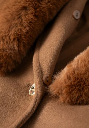 Cappotto di lana marrone con collo in pelliccia sintetica, caratterizzato da bottoni marroni e un dettaglio metallico, che mette in risalto texture morbide e tonalità calde.