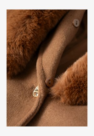 Cappotto di lana marrone con collo in pelliccia sintetica, caratterizzato da bottoni marroni e un dettaglio metallico, che mette in risalto texture morbide e tonalità calde.