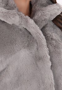 Cappotto grigio in pelliccia sintetica con una texture morbida, dotato di un ampio colletto e una finitura soffice, progettato per garantire calore e comfort.