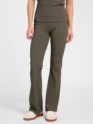 Vrouw draagt olijfgroene wijde broek en bijpassend kort mouwtopje, gecombineerd met crème- en beige sneakers, staand op een effen achtergrond.