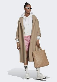 Abrigo beige, sudadera blanca con capucha, pantalones cortos rosas, gafas de sol blancas, bolsa de mano beige y zapatillas blancas con detalles negros. Calcetines a rayas blancas.