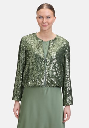 Groene bomberjack met pailletten en een ritssluiting aan de voorkant, met een cropped ontwerp en lange mouwen, gedragen over een bijpassende groene jurk.