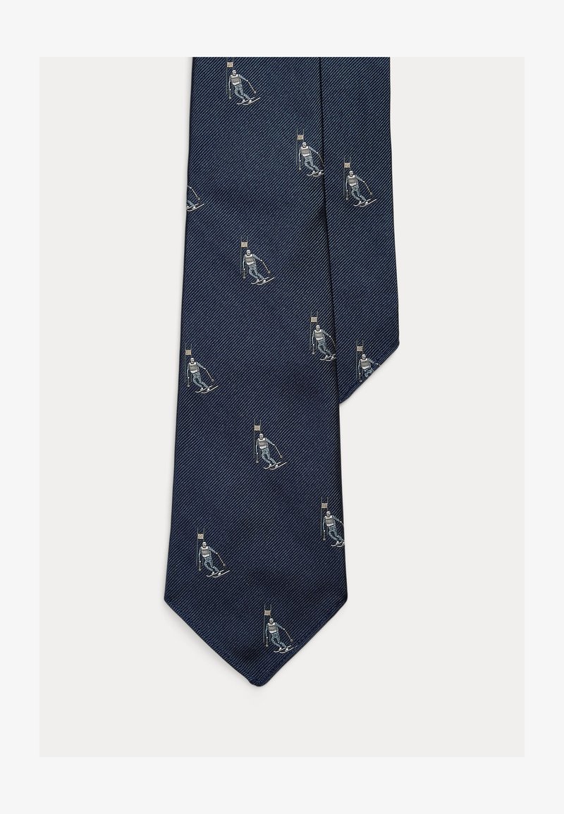 Tmavě modrá hedvábná kravata s rybí kostí vzorem a opakujícími se ilustracemi lyžaře v bílé a světle modré barvě, s designem s špičatým koncem.