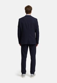 Completo blu scuro con una vestibilità su misura, caratterizzato da un blazer strutturato e pantaloni abbinati, abbinato a sneakers grigio chiaro per un tocco informale.