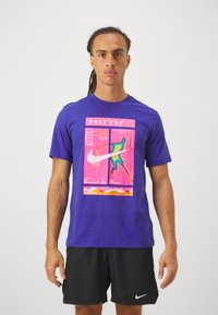 Μωβ μπλούζα Nike με μεγάλο, πολύχρωμο γραφικό που διαθέτει μια σιλουέτα και σχέδια. Κοντά μανίκια, χαλαρή εφαρμογή, κατασκευασμένη από αναπνέον ύφασμα.