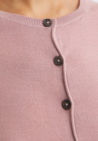 Cardigan tricoté rose pâle avec un col rond, une fermeture boutonnée devant avec deux boutons brun foncé, et des accents côtelés le long des bords.