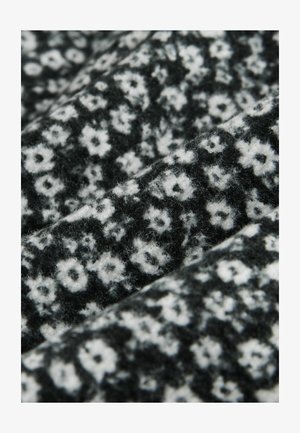 Tela negra con una superficie texturizada que presenta un patrón floral blanco. El diseño consiste en pequeñas flores dispersas y un sombreado sutil.