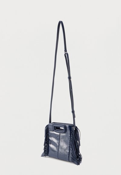 Τσάντα χιαστί σε ναυτικό μπλε χρώμα, κατασκευασμένη από γυαλιστερό υλικό με λεπτομέρειες κρόσσια στα πλαϊνά. Διαθέτει κοντή πάνω λαβή και ρυθμιζόμενο λουρί.