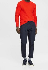 Czerwony sweter z prążkowanej wełny w połączeniu z granatowymi slim-fit spodniami. Obuwie to granatowe sneakersy z białymi podeszwami i szare skarpetki w paski.