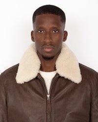 Chaqueta de cuero marrón con un suave cuello de borreguillo color crema, cierre de cremallera completa y un suéter de punto visible por debajo.