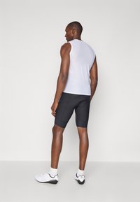 Enganliegendes, ärmelloses weißes Mesh-Top mit schwarzen Fahrradhosen. Das Top hat ein strukturiertes Muster, und die Hosen verfügen über flache Nähte. Weiße Sportschuhe.