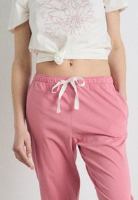 T-shirt bianco corto e leggero con disegno floreale rosa, abbinato a pantaloni jogger rosa con cordoncino, dotati di tasche laterali e texture liscia.