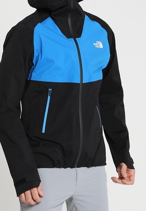 Schwarz-blaue North Face Kapuzenjacke mit Frontreißverschluss und Reißverschlusstaschen, getragen von einer Person mit hellgrauer Hose.