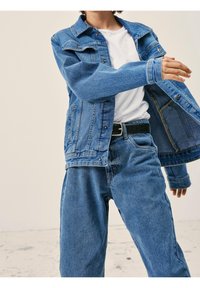 Pár modrých denimových džín a odpovídající denimová bunda se strukturovaným límcem, patentkami a předními kapsami, stylizované přes bílé tričko.