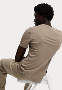 Camiseta de manga corta color caqui hecha de algodón suave, con un clásico cuello redondo y una textura suave y uniforme, vista desde un ángulo posterior.