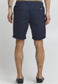 Shorts bleu marine avec ourlet roulé, ceinture élastique et deux poches arrière à bouton. Le matériau semble léger et texturé.