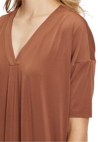 Brun V-ringad topp med korta ärmar, tillverkad av mjukt material. Har en löst sittande passform, subtil drapering och ren sömnad längs kanterna.