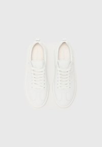 Baskets blanches avec une tige en cuir lisse, bout rond, design à lacets et détails de couture subtils. Comprend une petite languette à l'arrière.