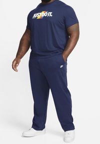 Námořnická modrá Nike tričko s multibarevným grafikou "JUST DO IT.", spárované s odpovídajícími námořnickými kalhotami a bílými teniskami.