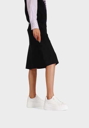 Sneakers platform bianchi con pannelli texturizzati e lacci, indossati con una gonna nera e una maglietta a maniche lunghe a righe.