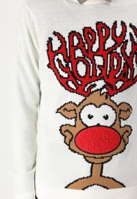 Suéter de punto blanco con un diseño de reno que tiene una nariz roja, ojos negros y una textura esponjosa. La frase "Felices Fiestas" en rojo y negro encima.