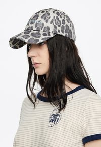 Gorra de béisbol de estampado de leopardo en denim gris y negro, con visera curvada y texto bordado. Camisa de algodón a rayas con acentos en azul marino.