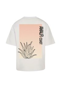 Tricou alb cu un grafic mare imprimat, cu un fundal în gradient piersică și un desen cu liniile negre al unei plante de agave, etichetat "COASTA AMALFIEI."