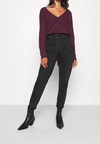 V-ringad långärmad vinröd tröja i kombination med högmidjade svarta jeans i denim och svarta anklestövlar med spetsiga tår och blockhär.