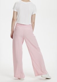 Světlé růžové kalhoty s širokými nohavicemi vyrobené z lehkého materiálu, doplněné jednoduchou bílou košilí s krátkým rukávem, která ukazuje uvolněný střih.