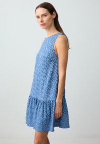 Abito blu senza maniche con pois bianchi, orlo a balze svasato e texture liscia. Collo rotondo semplice, lunghezza midi casual.