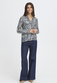 Blouse à manches longues avec un motif abstrait bleu marine et crème, assortie à un jean bootcut bleu foncé et des escarpins beige clair.