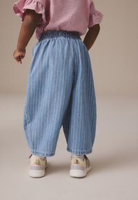 Lichtblauwe denimbroek met verticale witte strepen, elastische tailleband en een relaxte pasvorm. Gepaard met multicolore sneakers met een dikke zool.