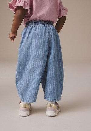 Lichtblauwe denimbroek met verticale witte strepen, elastische tailleband en een relaxte pasvorm. Gepaard met multicolore sneakers met een dikke zool.