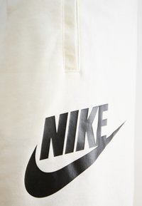 Gräddfärgad tyg har en framträdande svart Nike-logotyp och swoosh-design, med en slät textur och minimal sömnadsdetalj.