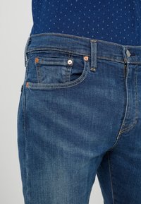 Blå denimjeans med en klassisk design, utrustade med koppardetaljer, fem fickor och subtil blekning vid låren.