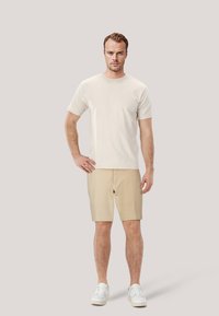 Ljusbeige t-shirt med kort ärm, matchad med khakifärgade shorts och vita sneakers, med en enkel design och avslappnad passform.
