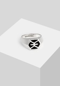 Bague en argent avec un design hexagonal comprenant un inlay en émail noir et un motif géométrique. Le texte gravé indique "KUZZOÍ."
