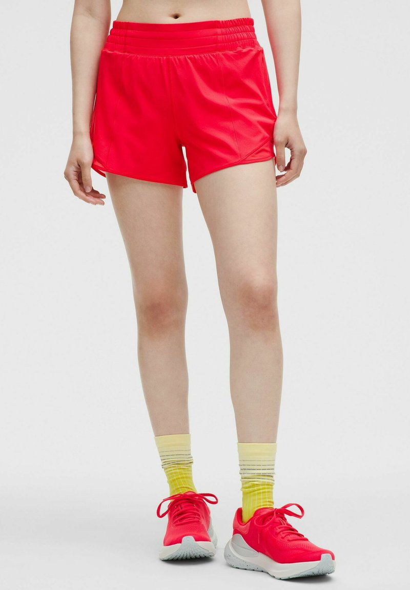Pantalones cortos deportivos rojos con una cintura elástica, tela suave y un ajuste relajado. Acompañados de calcetines amarillos a rayas y zapatillas deportivas.