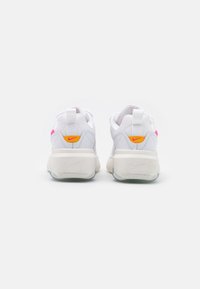 White Nike sneakers with a textured mesh upper, pink and orange accents, padded collar, and a thick cream-colored sole with a translucent base.