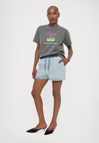 Grå t-skjorte med fargerik "Moschino Jeans" tekst, sammen med lyseblå denimshorts og svarte spisse mules. Stilfullt og uformelt utseende.