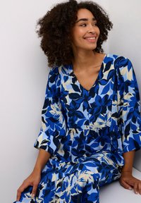 Blomsterprint kjole i nuancer af blå og creme, med V-udskæring, puffærmer og en lagdelt nederdel for ekstra volumen og struktur.