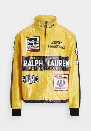 Gelbe, strukturierte Rennjacke mit mehreren aufgedruckten Logos und Aufnähern, schwarzen Akzenten an Ärmeln und Bündchen, mit durchgehendem Reißverschluss.