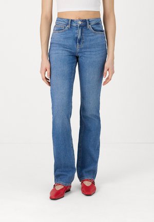 Light blue flared jeans with a high waist, five-pocket design, and contrast stitching. Fabric has a smooth texture. Paired with red shoes.
